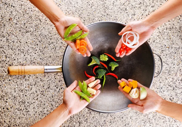 Four hands puts fresh vegetables in the wok. Cooking concept