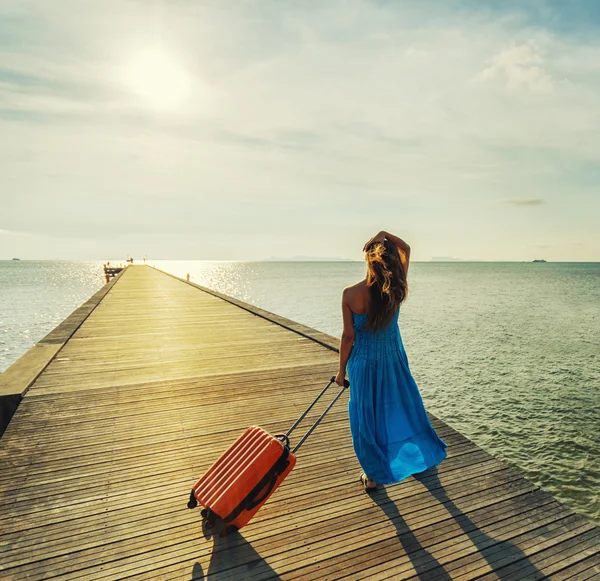 Young woman with suitcase waking on wooden pier
