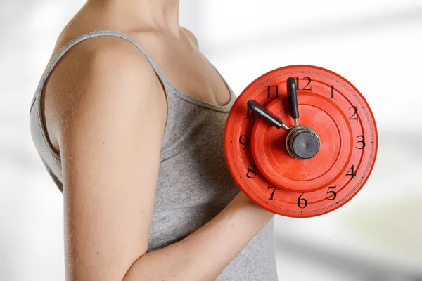 Beginner female athlete holding dumbbell with clock dial. Time f