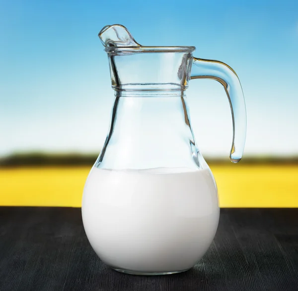 Jug of milk on meadow background. Half full pitcher