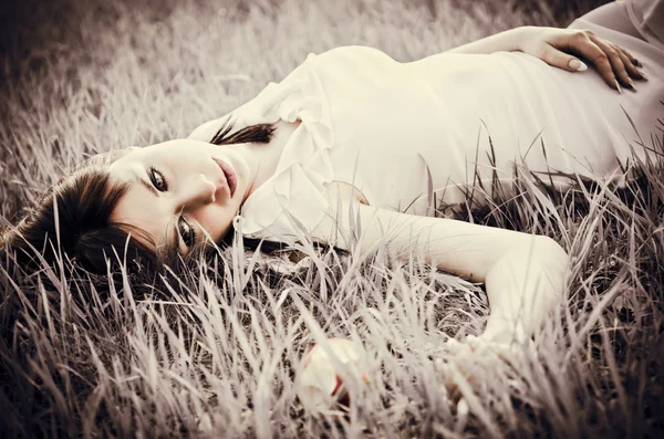 Sad beautiful girl lying on grass. Faded effect