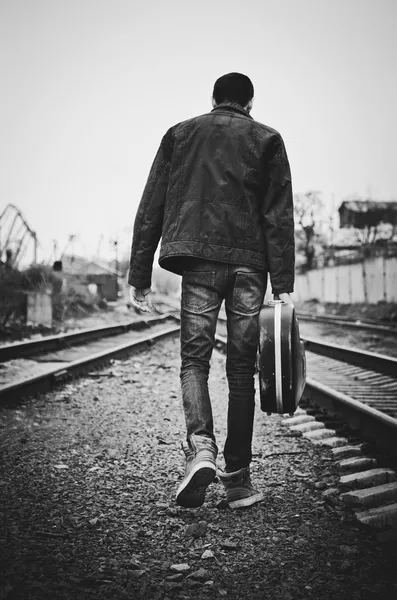 Young man with guitar case in hand is going away. Rear view, black and white