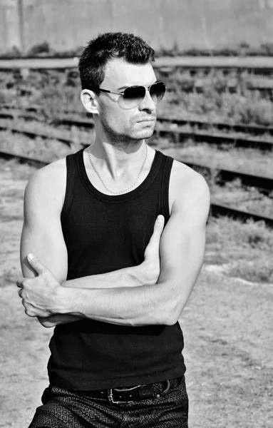 Fashion shot: portrait of handsome young man in black shirt wearing sunglasses. Black and white