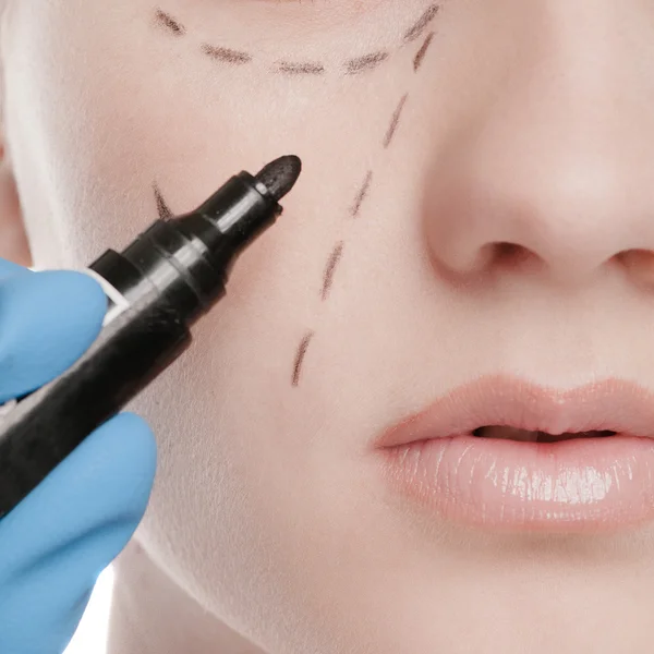 Beautician draw correction lines on woman face