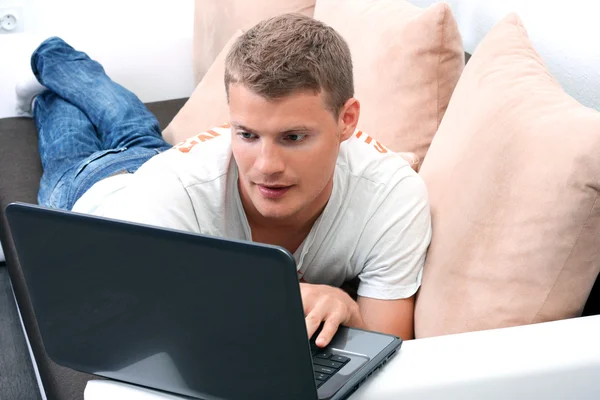 Young man laying on sofa and using laptop