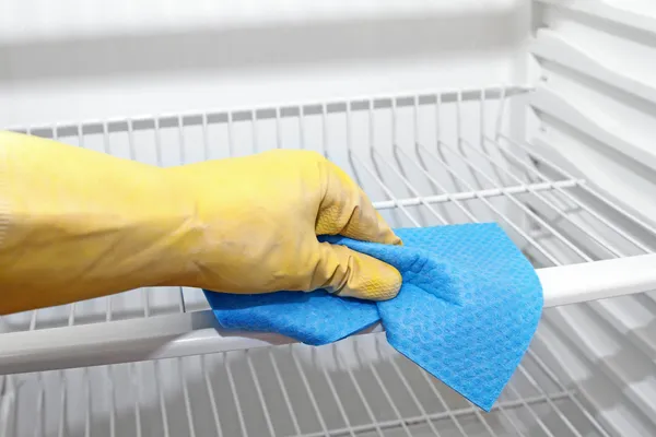 Hand with yellow protective glove cleaning refrigerator