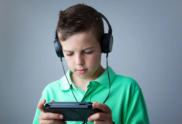 Boy playing game console against grey background