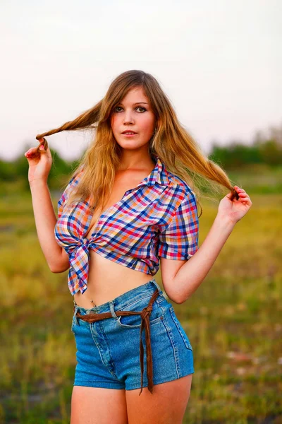Young woman blonde in plaid shirt, denim shorts at sunset, flowi