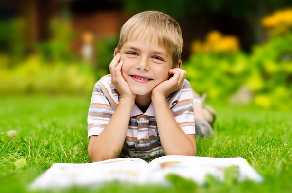 Beauty smiling child boy reading book outdoor on green grass fie