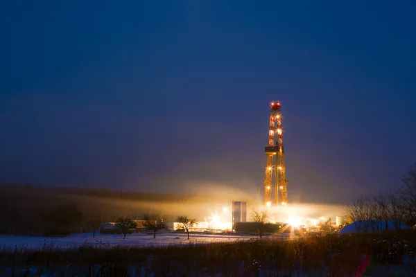 Oil well in the snowy landscape lit up at night.