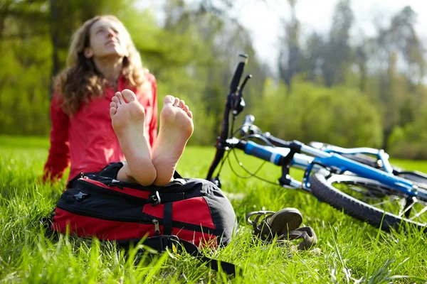 Happy girl cyclist enjoying relaxation sitting barefoot in spring park
