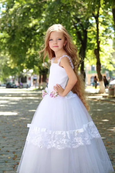 Charming young girl with long healthy hair in a beautiful white dress walking outdoors