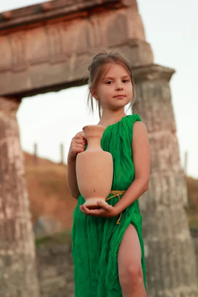 Joyful smiling girl in a beautiful emerald green dress with an amphora in the role of the Greek goddess.