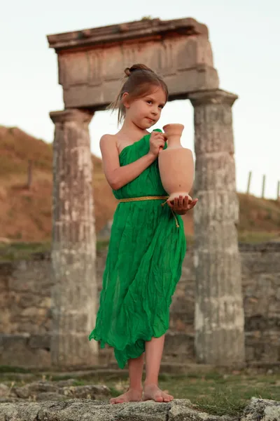 Beautiful young Greek goddess in emerald green vintage dress holding of an ancient amphora.