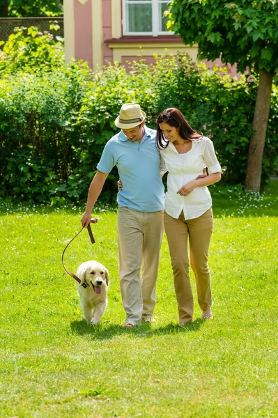 Happy couple walking dog on park lawn