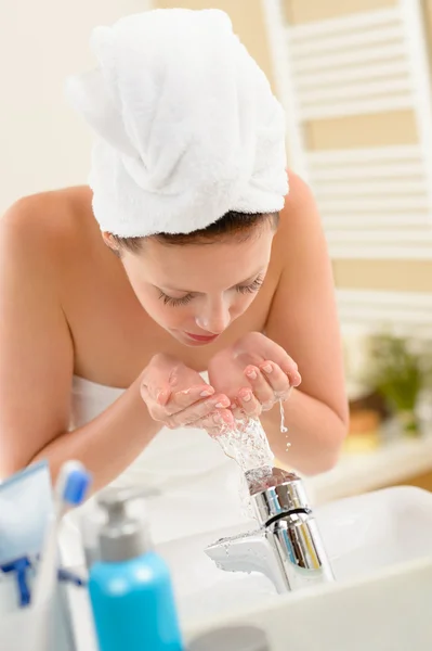 Woman washing face above bathroom sink