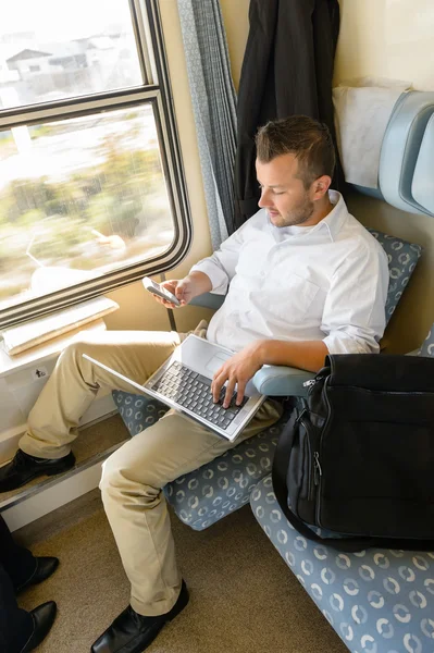 Man texting on phone holding laptop train