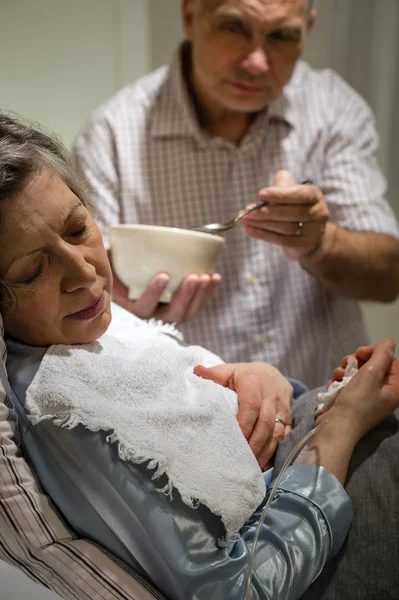 Mature man helping ill wife feeding soup