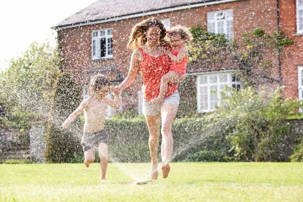 Mother And Two Children Running Through Garden Sprinkler