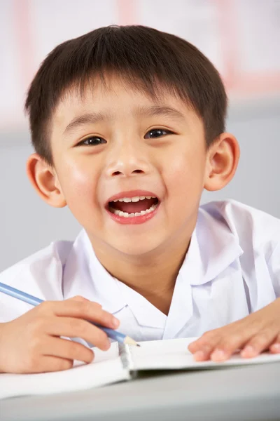 Male Student Working At Desk In Chinese School Classroom