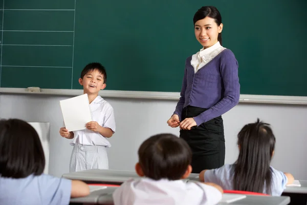 Pupil And Teacher Standing By Blackboard In Chinese School Class