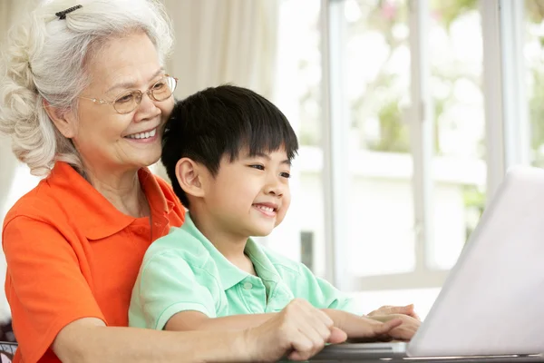 Chinese Grandmother And Grandson Sitting At Desk Using Laptop At