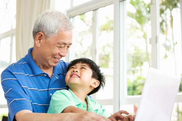 Chinese Grandfather And Grandson Sitting At Desk Using Laptop At