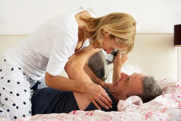Senior Couple Fooling Around Together In Bed Whilst Man Reads Newspaper