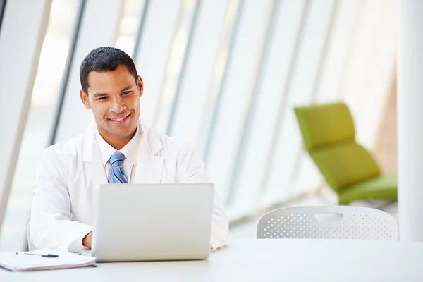 Doctor Using Laptop Sitting At Desk In Modern Hospital