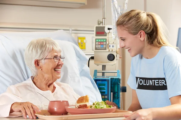 Teenage Volunteer Serving Senior Female Patient Meal In Hospital