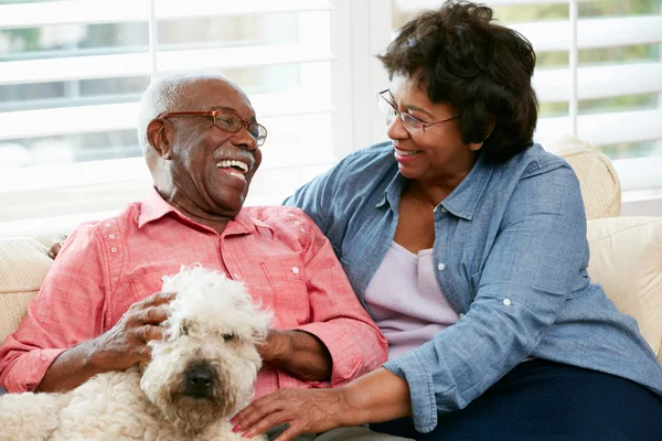 Happy Senior Couple Sitting On Sofa With Dog