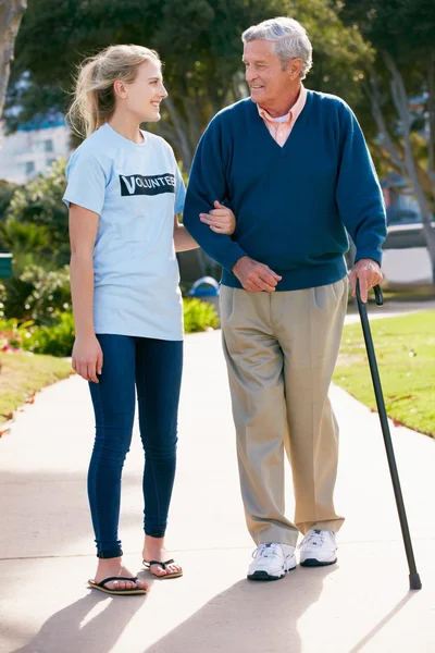 Teenage Volunteer Helping Senior Man Walking Through Park