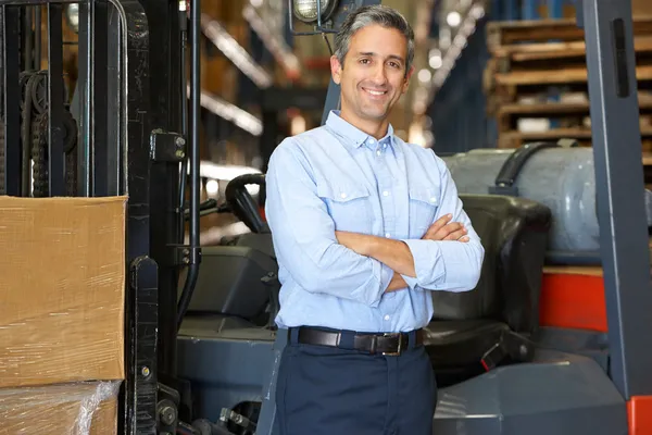 Portrait Of Man With Fork Lift Truck In Warehouse