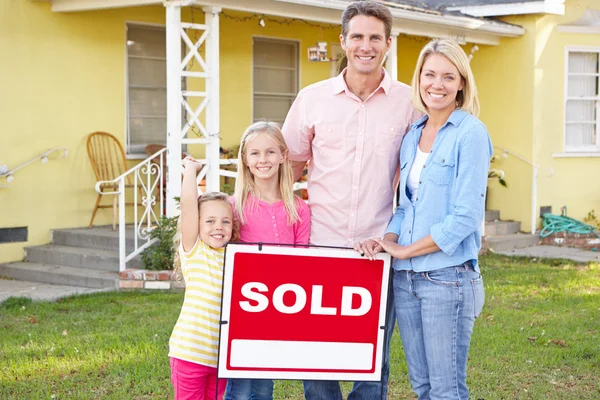 Family Standing By Sold Sign Outside Home