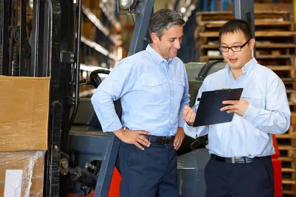 Businessmen Meeting By Fork Lift Truck In Warehouse