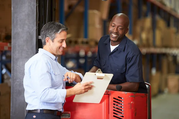 Fork Lift Truck Operator Talking To Manager In Warehouse