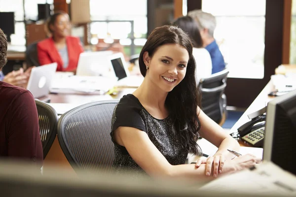 Businesswoman Working At Desk With Meeting In Background