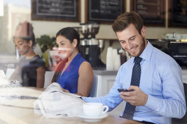 Businessman With Mobile Phone And Newspaper In Coffee Shop