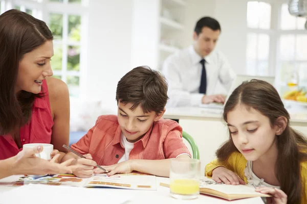 Mum Helps Children With Homework As Dad Works In Background