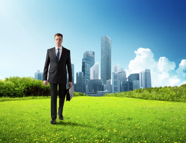 Business man walking on green field and modern city