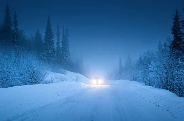 Lights of car and winter road in forest