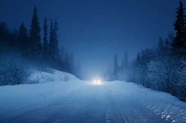 Lights of car and winter road in forest