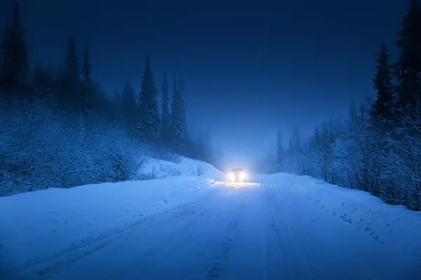 Lights of car and winter road in forest