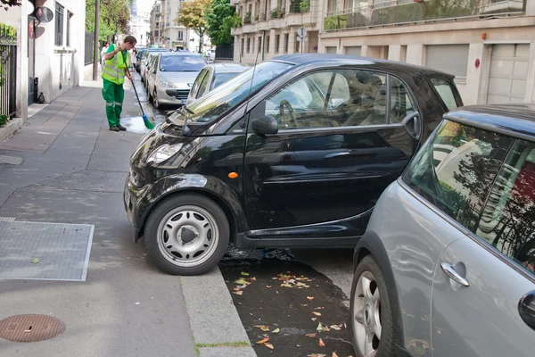 PARIS - JULY 14: An unidentified man sweeping the sidewalk next to parked cars in Paris, July 14, 2011.