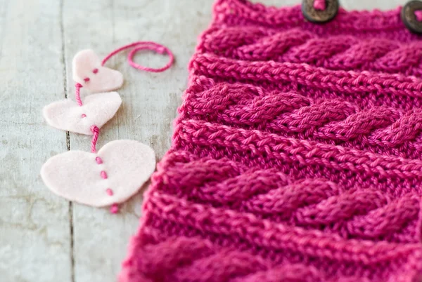 Knitting pattern and felt hearts on a wooden background