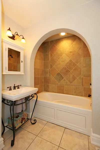 Tub with arch and stone tiles and sink bathroom design.