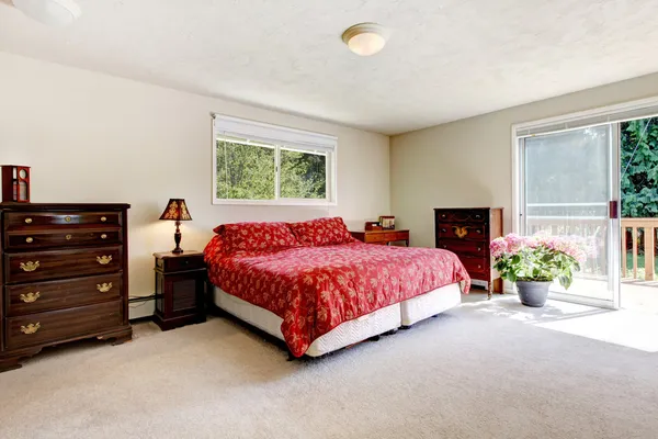 Bedroom with red bed, open balcony door and beige walls.