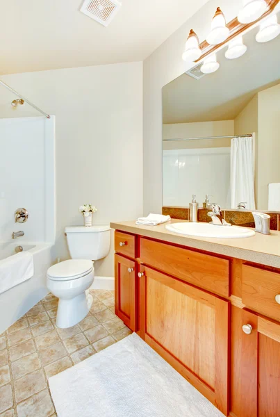 Bathroom with white tub, toilet and sink and wood cabinets.