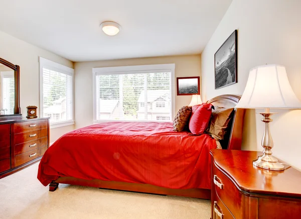 Bedroom with two windows and red bed with wood furniture.