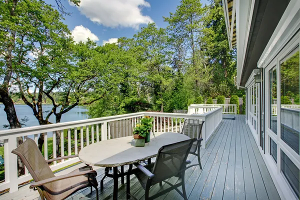 Large long balcony home exterior with table and chairs, lake view.